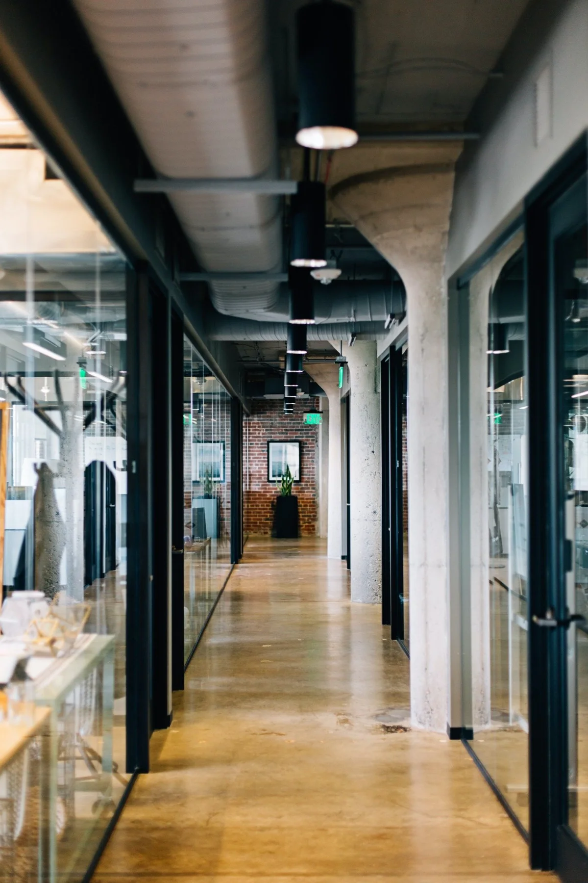 A light-filled workspace with glass offices and a long wood-floored corridor